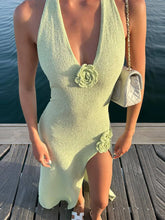 Woman wearing a light green dress with floral details on a wooden dock by water.